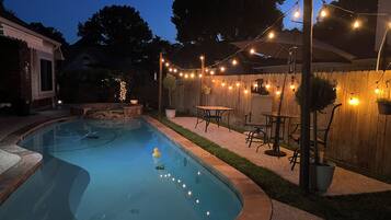 A backyard with a swimming pool, outdoor furniture, and string lights.