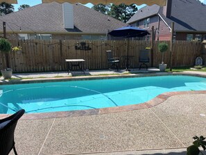 A backyard with a swimming pool, a wooden fence, outdoor furniture, and a patio area.