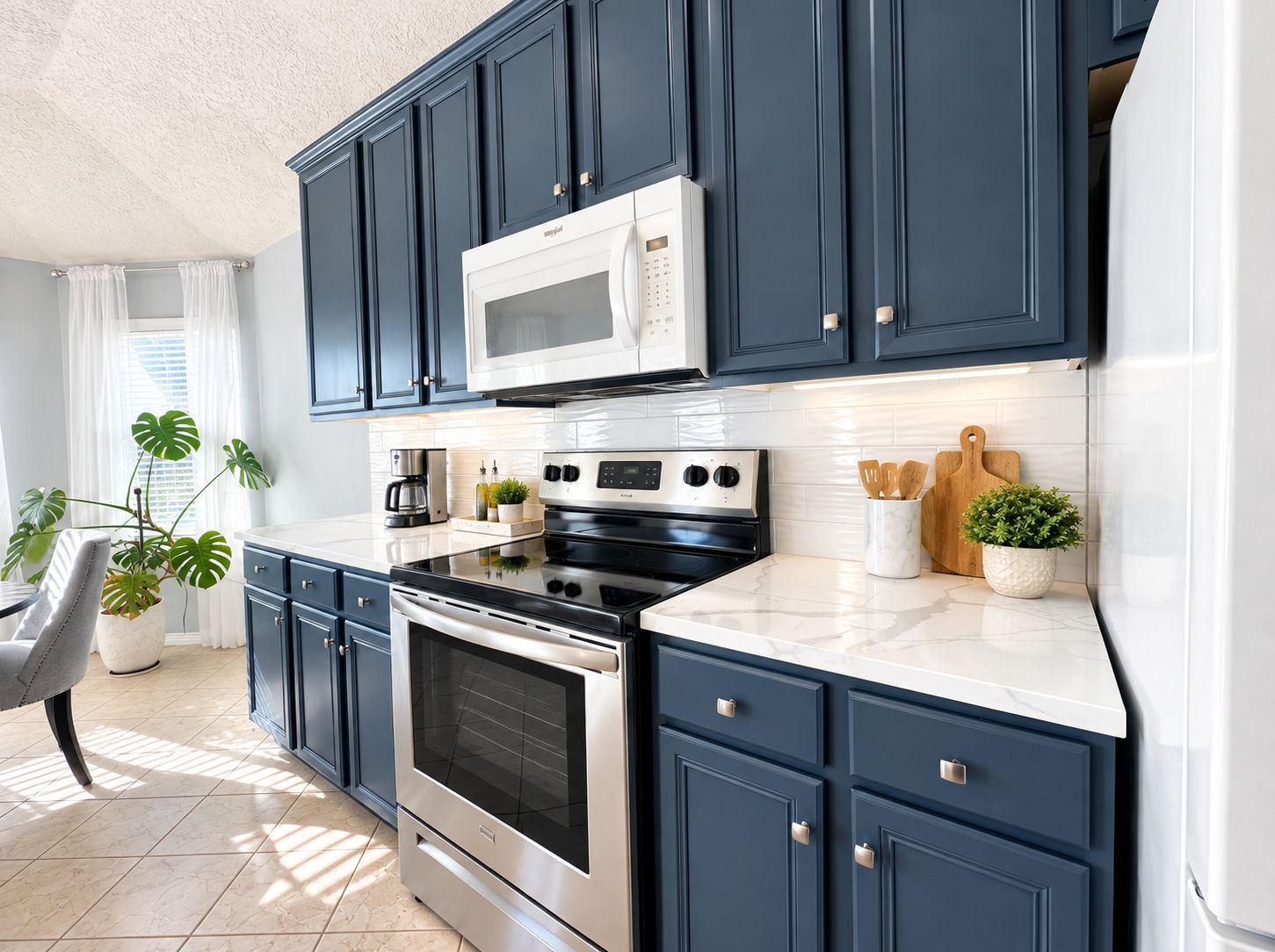 Una cocina moderna con armarios azul oscuro, electrodomésticos de acero inoxidable y encimera blanca.