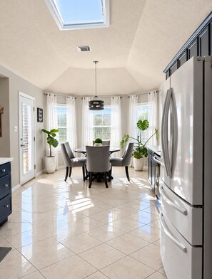 A modern kitchen with a large refrigerator, a dining area with a table and chairs, and potted plants.