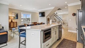 A modern kitchen with a central island, stainless steel appliances, and a dining area with a sofa and chairs. - Waterfront Condo w/ Rooftop Deck & Beach Access (Fenwick Island)