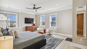 A bedroom with a large bed, a ceiling fan, a TV, and a view of the outside. - Waterfront Condo w/ Rooftop Deck & Beach Access (Fenwick Island)