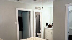 A bedroom with a bed, a ceiling fan, a bathroom visible through an open door, and a sign above the door.