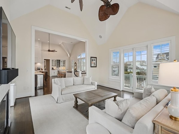 A spacious living room with a fireplace, a dining area, and a kitchen visible through an open doorway.