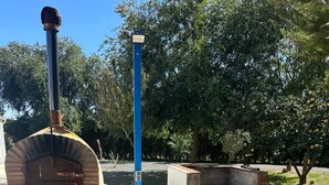 Forno per pizza in mattoni con canna fumaria, un palo blu e un’area salotto con una panchina.