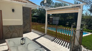 Una veranda con un tavolo in vetro e sedie in metallo, una recinzione in legno e una piscina sullo sfondo.