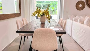 A dining area with a long table, chairs, a vase of flowers, and a white sofa. - Elegant Flat in the Center of Glyfada (Glifada)