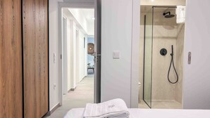 A hotel room with a wooden wardrobe, a bed with neatly folded towels, and a glass-enclosed shower area. - Elegant Flat in the Center of Glyfada (Glifada)