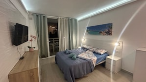 Une chambre à coucher avec un lit, une télévision, une plante et un tableau au mur.