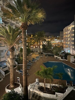 A pool area with lounge chairs, palm trees, and a swimming pool surrounded by buildings. - Ponderosa Las Americas (Costa Adeje)