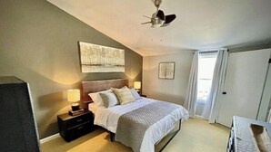 Une chambre à coucher avec un lit, des tables de chevet, un ventilateur de plafond et une grande fenêtre.