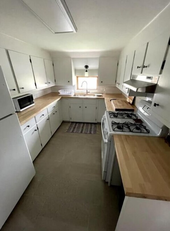 Una cocina compacta con armarios blancos, una encimera de madera, un fregadero y una estufa.