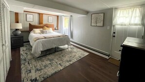 A bedroom with a bed, nightstand, and a window with curtains. - Cozy Cuddler's Cottage (West Falls)