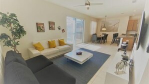 A modern living room with a sofa, coffee table, and a dining area with chairs and a table.