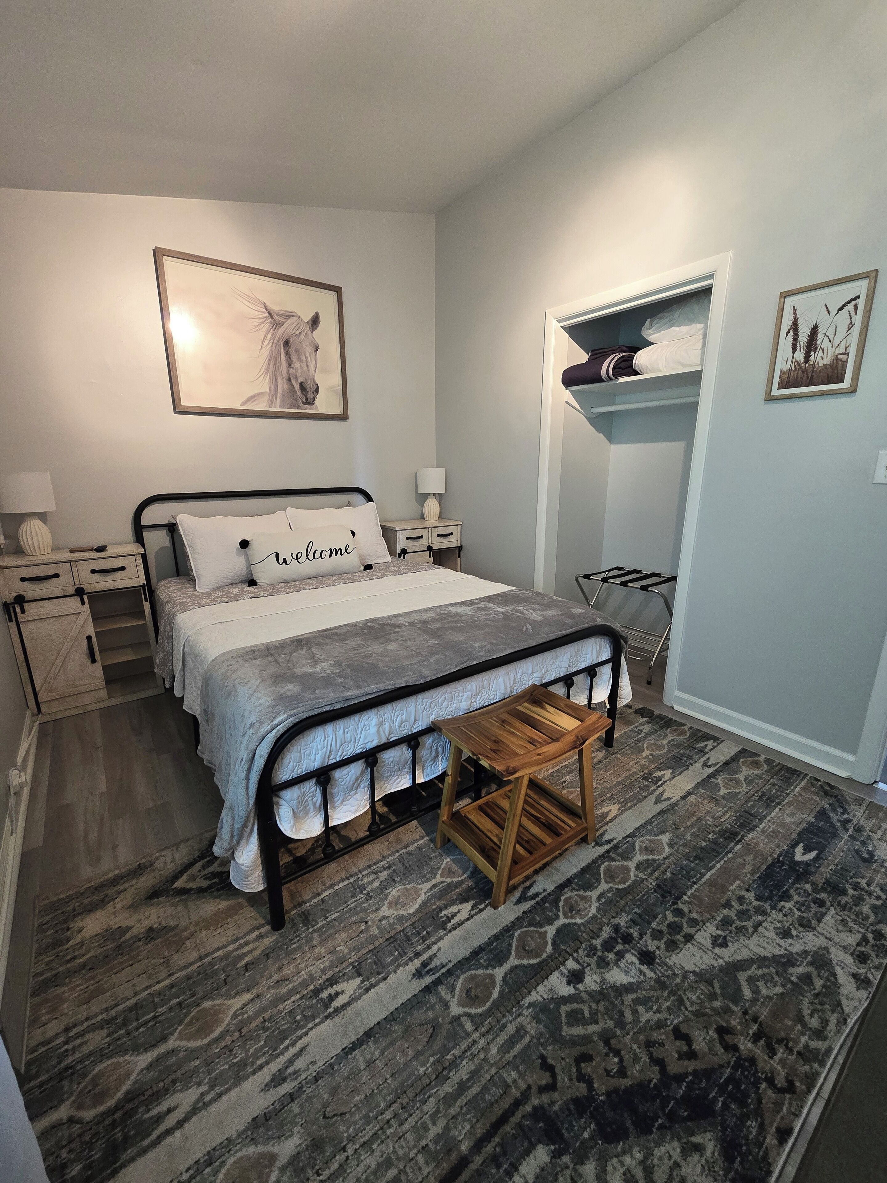 A bedroom with a bed, bedside tables, a nightstand, a wooden stool, a patterned rug, and a wardrobe.