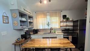 Une cuisine avec une table en bois, des chaises noires, un four encastré et un réfrigérateur.