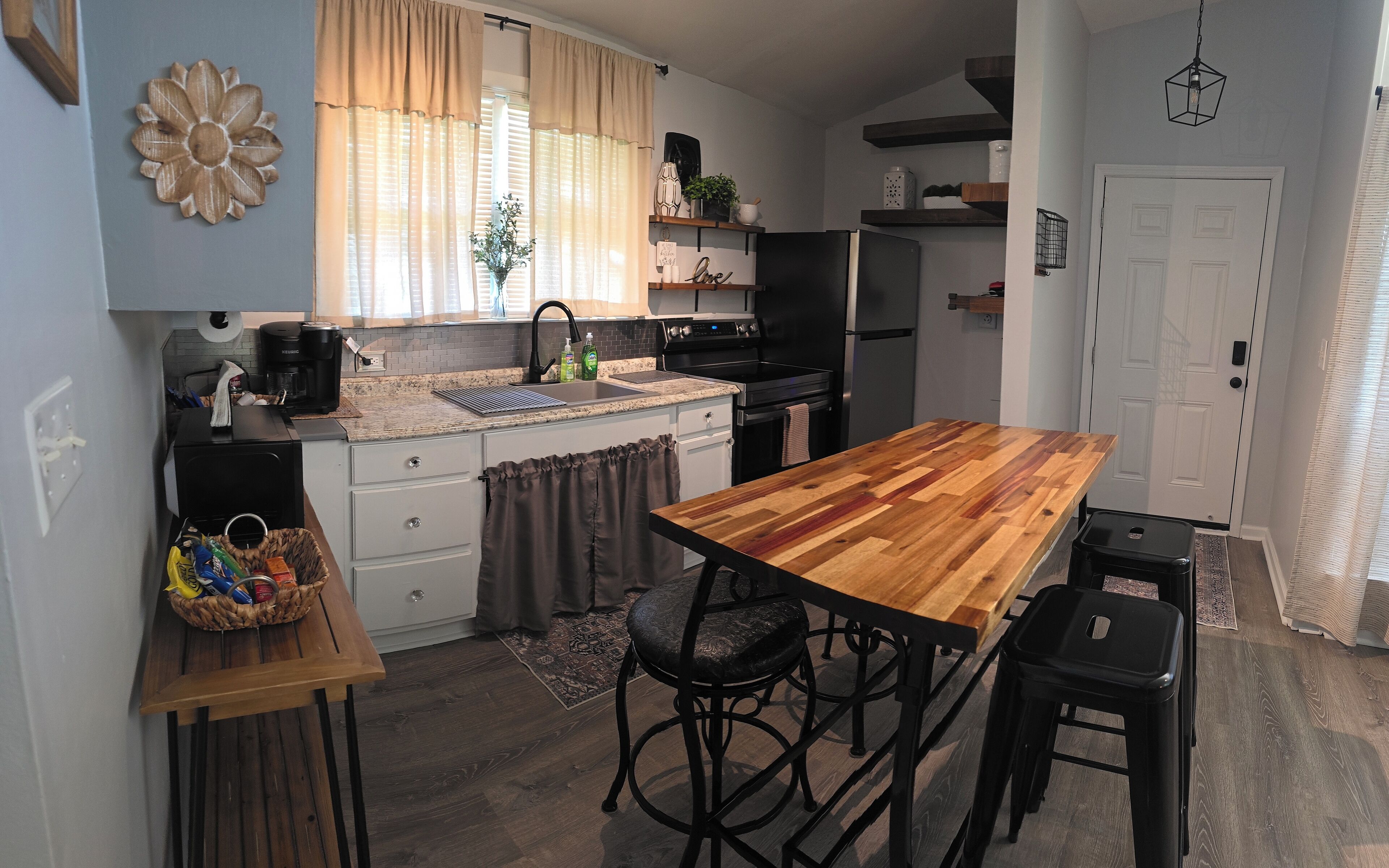 Cocina compacta con una isla de madera, taburetes de bar y un refrigerador.