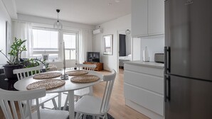 A modern kitchen with white cabinetry, a large refrigerator, and a dining area with a white table and chairs.