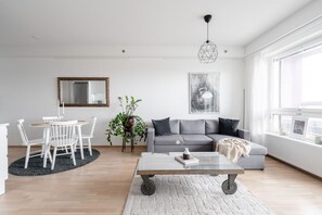 Una sala de estar moderna con un sofá gris, una mesa de comedor redonda con sillas, una mesa de centro, una planta en maceta y un ventanal con vistas.