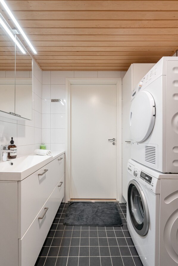 A compact laundry room with a washing machine, a dryer, a sink, and a mirror.