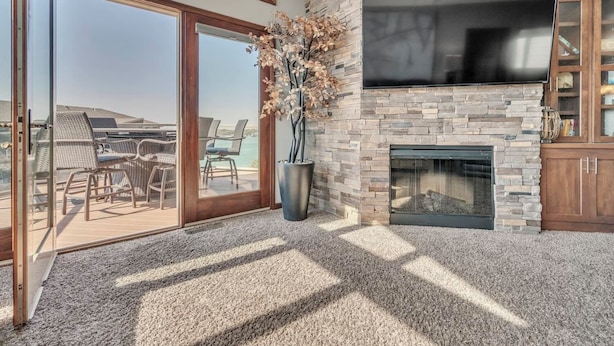 A modern outdoor living area with a stone fireplace, a flat-screen TV, and a glass door leading to a patio with outdoor furniture.