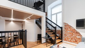 A spacious loft apartment with a wooden floor, a dining area, a staircase, and a brick wall.