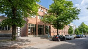 A building with large windows and a brick facade, parked cars along the street, and trees lining the sidewalk.