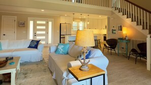 A spacious living room with a high ceiling, a staircase, and a kitchen in the background. - Spacious 6-bedroom house for Masters week; Lake, golf and lake views! (Greensboro)
