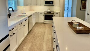A modern kitchen with white cabinetry, a central island, and a microwave. - Spacious 6-bedroom house for Masters week; Lake, golf and lake views! (Greensboro)