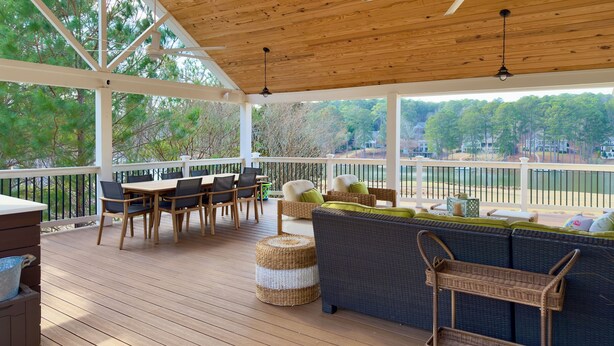 A covered outdoor deck with wooden flooring, a ceiling fan, and a view of a lake and trees. - Spacious 6-bedroom house for Masters week; Lake, golf and lake views! (Greensboro)