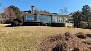 A two-story house with large windows, a covered porch, and a well-maintained lawn. - Spacious 6-bedroom house for Masters week; Lake, golf and lake views! (Greensboro)