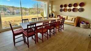 A dining area with a large table and chairs, a sofa, and a view of a lake and houses. - Spacious 6-bedroom house for Masters week; Lake, golf and lake views! (Greensboro)