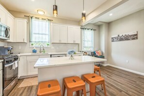 A modern kitchen with white cabinets, a large island, and orange stools.