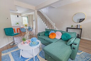 A modern living room with a green sofa, colorful cushions, a white coffee table, and a staircase leading to another level.