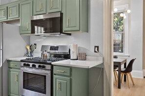 Cook your favourite meals in the charming kitchen, featuring a stainless steel gas stove, microwave, ample counter space, and beautiful green cabinetry.