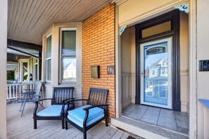 A porch with outdoor seating, a door with a number plate, and a brick wall.