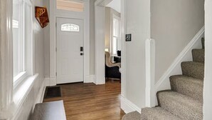 A hallway with a wooden floor, white walls, a white door with a window, and a staircase with patterned carpet. - 5BDRM GEM with Arcade - Mt Wash (Pittsburgh)