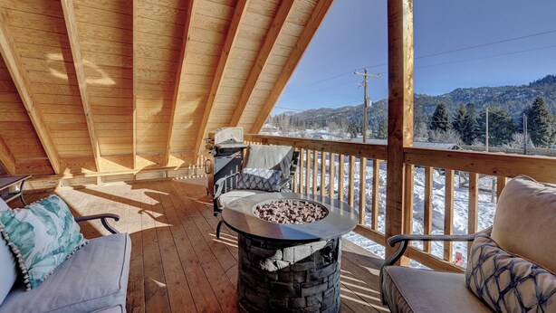 A wooden deck with a stone fire pit, outdoor seating, and a view of a snowy landscape. - Sleeps 29!  9-bedroom 8-Bath 3-Kitchen, Historic McBride Farm in Garden Valley (Garden Valley)
