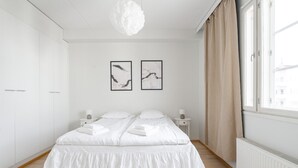 A bedroom with a large bed, white wardrobe, two bedside tables, a hanging light fixture, and two framed pictures on the wall. - 2BR Lakefront Home near Railway Station & Downtown (Jyväskylä)