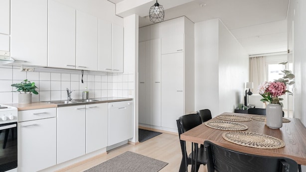 A modern kitchen with white cabinets, a wooden countertop, and a dining area with a table and chairs. - 2BR Lakefront Home near Railway Station & Downtown (Jyväskylä)