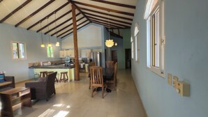 A spacious living area with a high ceiling, a kitchen in the background, and a dining area with wooden furniture. - 3-bedroom house in Cool Manzano Número 1 with large pool steps to the Pacific. (El Manzano Número 1)