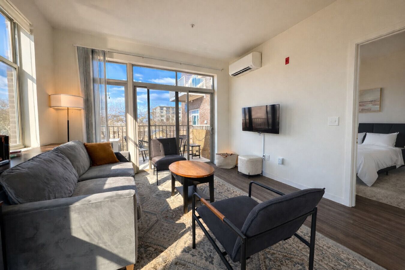 Un salon moderne avec un canapé, des fauteuils, une table basse, un téléviseur et un balcon offrant une vue agréable.