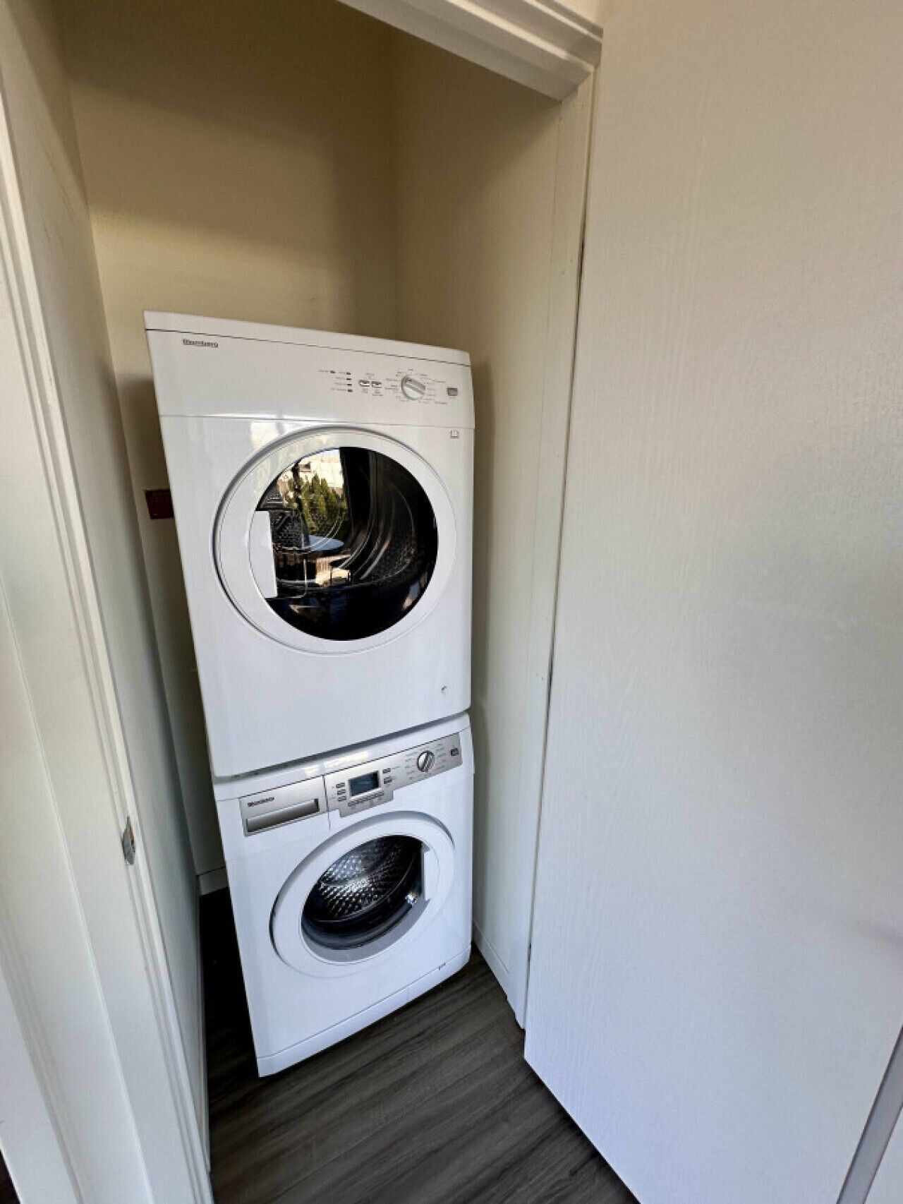 Una unidad compacta y blanca de lavadora y secadora instalada en la pared en un estrecho pasillo con piso de madera.