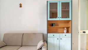 En beige sofa med pude, et lyseblåt skab med glasdøre og træhylder, samt en lille genstand på væggen.