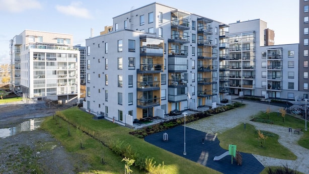 Ein modernes Mehrfamilienhaus mit mehreren Balkonen, einem Innenhof und einem Spielplatz.