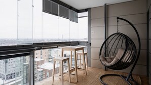 Un balcon avec un fauteuil suspendu, une petite table et deux tabourets.