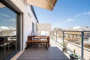 A balcony with a table and chairs, a stone wall, and a view of buildings.
