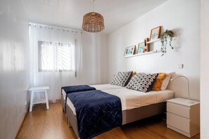 A bedroom with a bed, bedside tables, a desk, and a hanging light fixture.