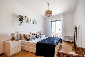 A modern bedroom with a bed, bedside tables, a hanging plant, and a view of the outdoors.