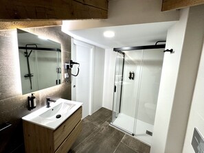 A modern bathroom with a white sink, wooden vanity, and a glass shower enclosure. - CavaBajaSuites 401 PALACIO REAL (Madrid)